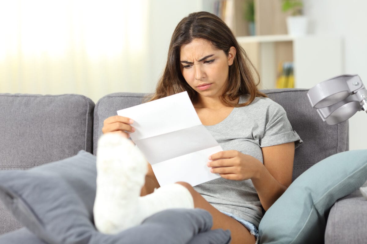 Worried injured woman reading a letter sitting on a couch in the living room at home after being denied workers comp claims