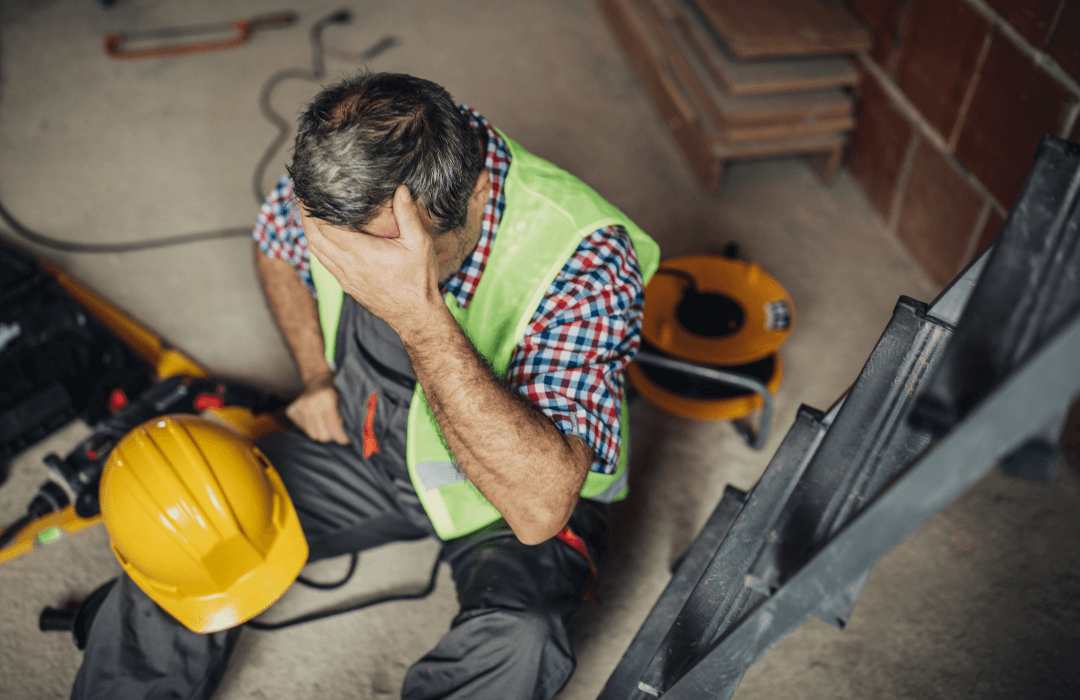 Construction worker sitting on the ground holding his head after a workplace injury, representing the importance of workers’ compensation in Pennsylvania.