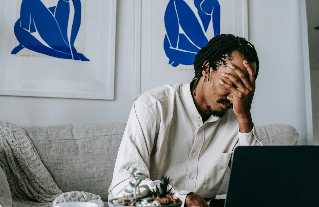 Frustrated worker sitting at home with hand on face while looking at laptop, representing common mistakes that can ruin a Pennsylvania workers’ compensation case.