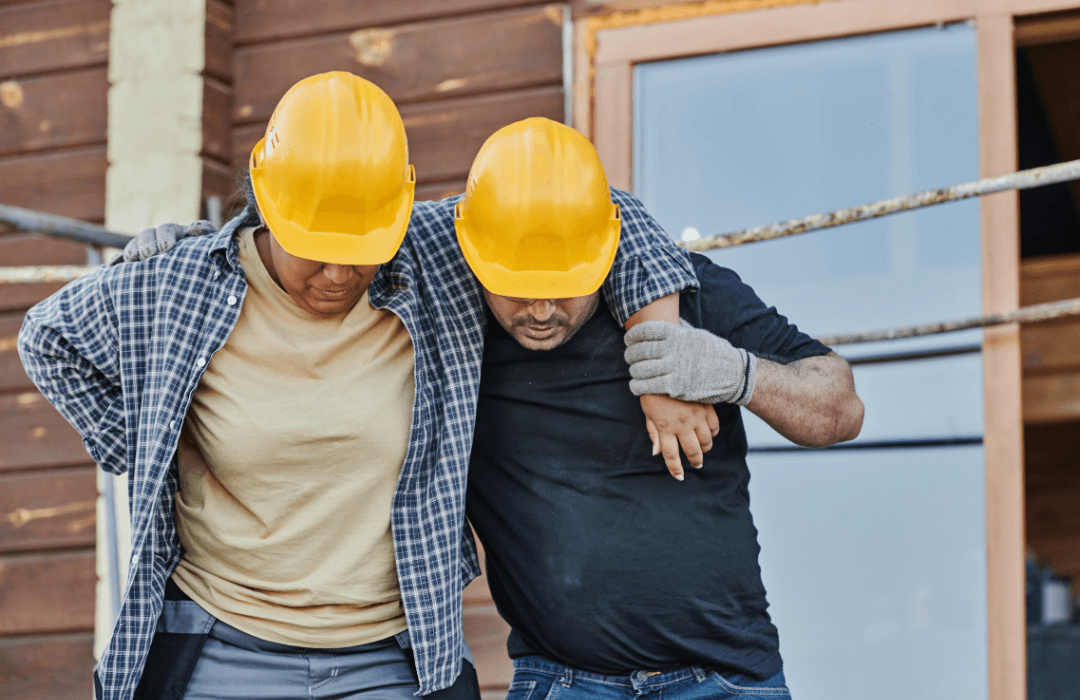 Two construction workers wearing yellow hard hats, one helping the other with an injury, representing situations not covered under Pennsylvania workers’ compensation.